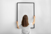 Frau hält leeren Bilderrahmen vor weiße Wand 