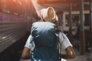Mann mit Rucksack und Strohhut geht neben einem Zug auf dem Bahnhof
