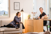Frau sitzt auf Couch und spricht mit Mann der am Esstisch sitzt David