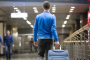 Mann mit Rücken zur Kamera zieht Koffer hinter sich im Flughafen
