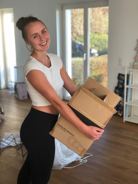 Frau hält Kartonbox und lächelt in die Kamera