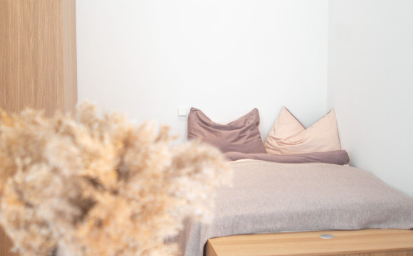 Ein minimalistisches Schlafzimmer mit einem Bett, das ein braunes Laken, eine beige Strickdecke und zwei Kissen in Beige und Braun hat.