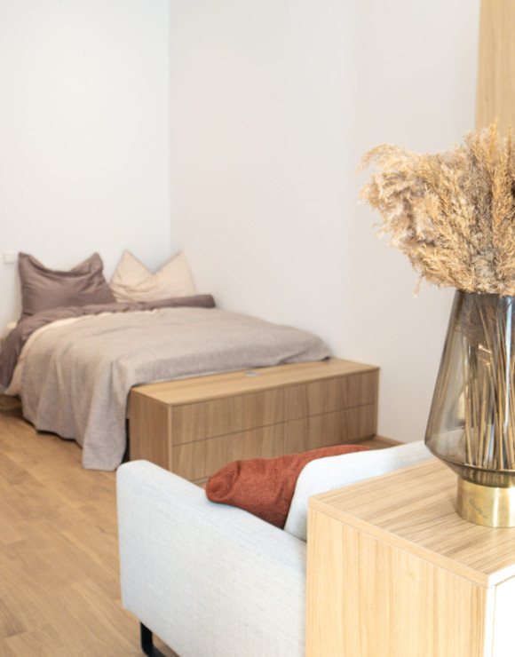 Ein modernes Schlafzimmer mit einem Bett, einem Nachttisch und einer Kommode, ergänzt durch stilvolle Dekorationselemente und Holzverkleidungen.
